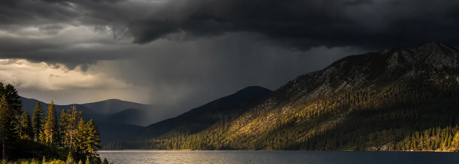 Storm cloud building over the ridges above the lake while sunlight still catches the water