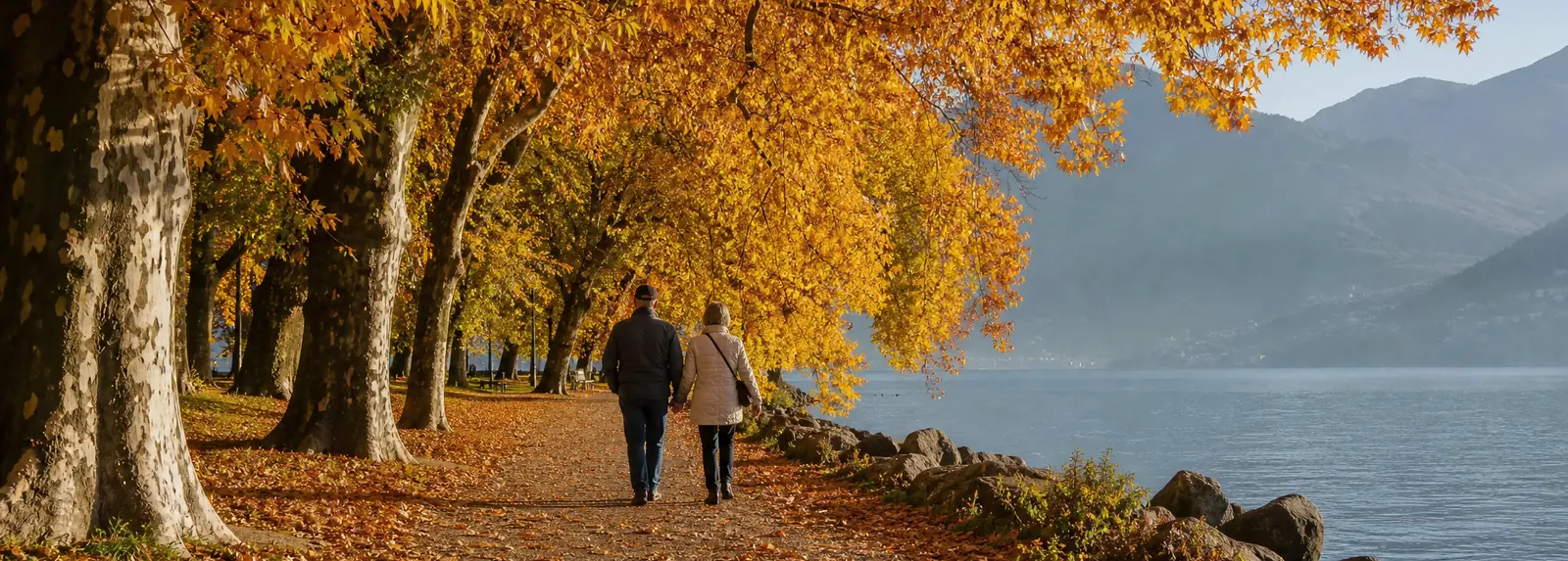 An avenue of trees in full autumn gold along a lakeside path, two people walking away