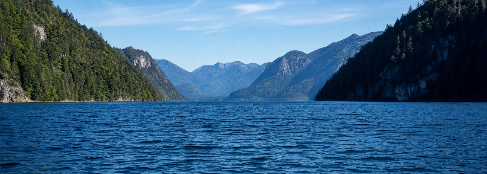 Eaux bleues profondes vues depuis un bateau, avec des pentes boisées escarpées plongeant vers le rivage